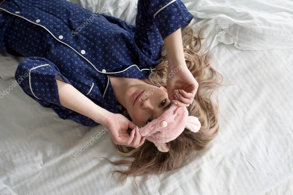 Cute blonde in her bed in blue pajamas and sleep mask, top view