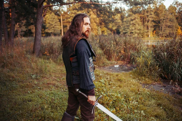 Ritari metsässä. Mies keskiaikaisessa asussa miekan kanssa. — kuvapankkivalokuva
