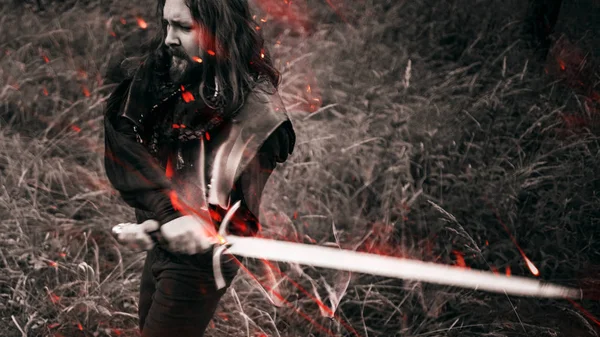 Batalla. Caballero en el bosque. Un tipo en traje medieval con una espada, efecto de fuego y tonificación — Foto de Stock