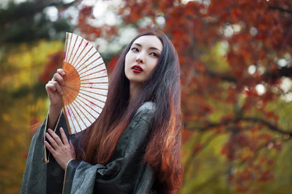 Hermosa joven mujer asiática con ventilador en el fondo de arce rojo — Foto de Stock
