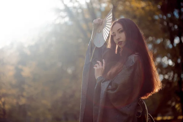 Retrato de jóvenes bellos asiáticos en kimono gris y con un ventilador, al aire libre — Foto de Stock