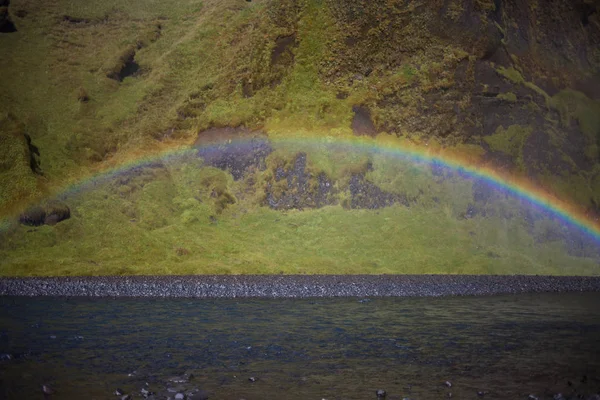 Regnbåge på bakgrunden av stenar, foten av Skogafoss vattenfall, Island — Stockfoto