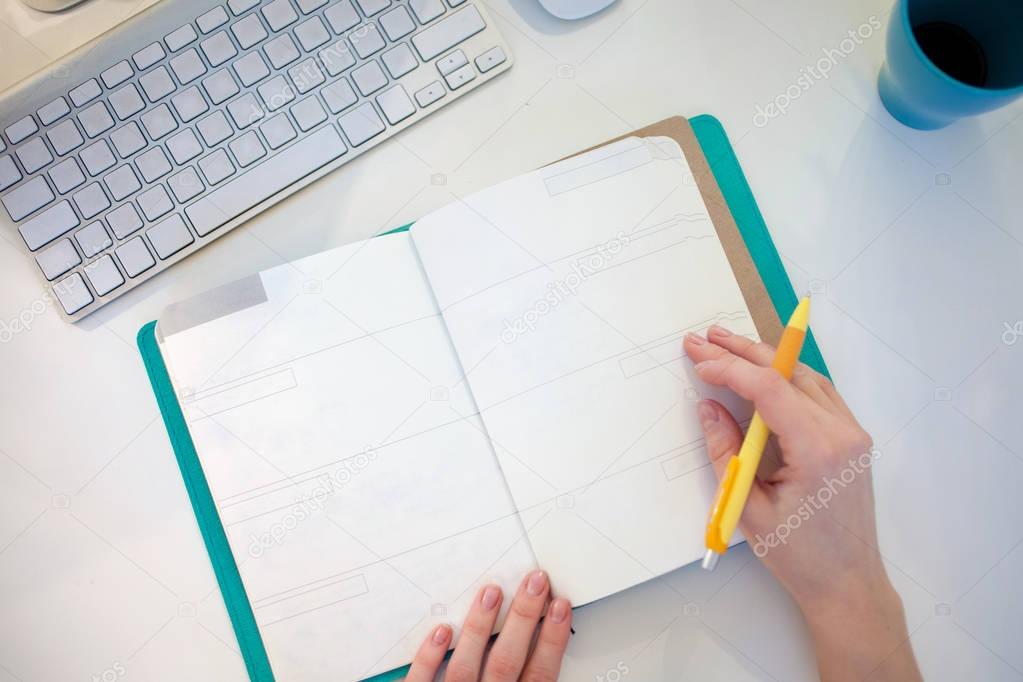 Young businesswoman sitting at desk and working. Beautiful woman fills planner, view from the top