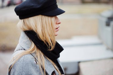 Genç, kalça ve çekici sarışın kız şık bir şapka ve gri bir ceket şehirde yürüyüş