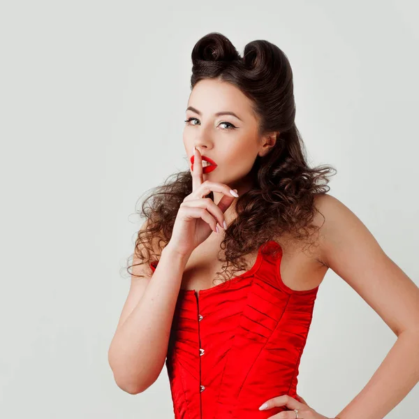 Charming lady in red corset, pin-up hairstyle. Finger at lips, Shh — Stock Photo, Image