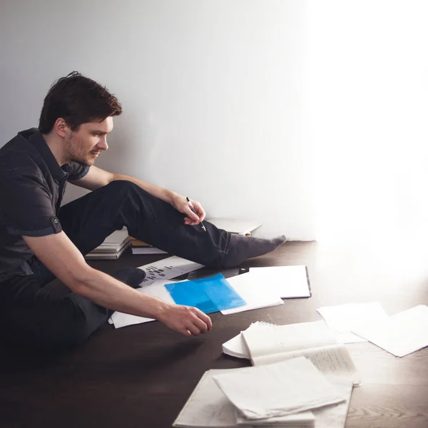 Fiatal férfi vállalkozó teszi, brainstorming, a lakásban a padlón ül. Kreatív megközelítés to business — Stock Fotó