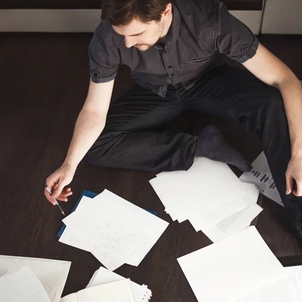 Joven empresario masculino hace una lluvia de ideas sentado en el suelo en el apartamento. Enfoque creativo de las empresas — Foto de Stock