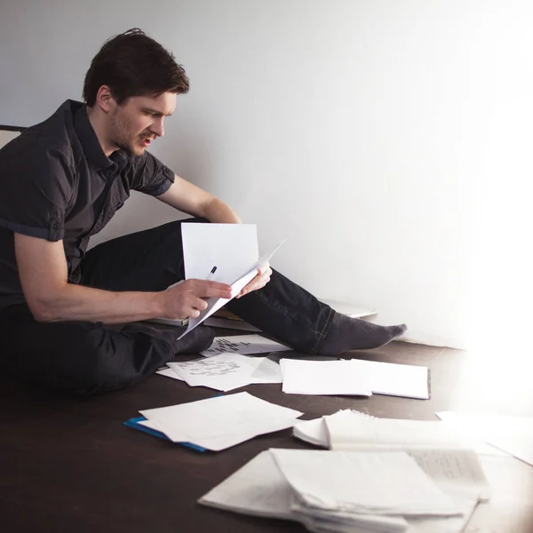 Joven empresario masculino hace una lluvia de ideas sentado en el suelo en el apartamento. Enfoque creativo de las empresas —  Fotos de Stock