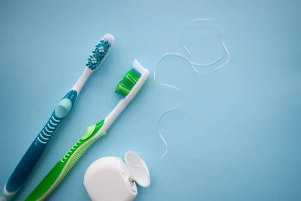 Dos cepillos de dientes y hilo dental sobre fondo azul —  Fotos de Stock