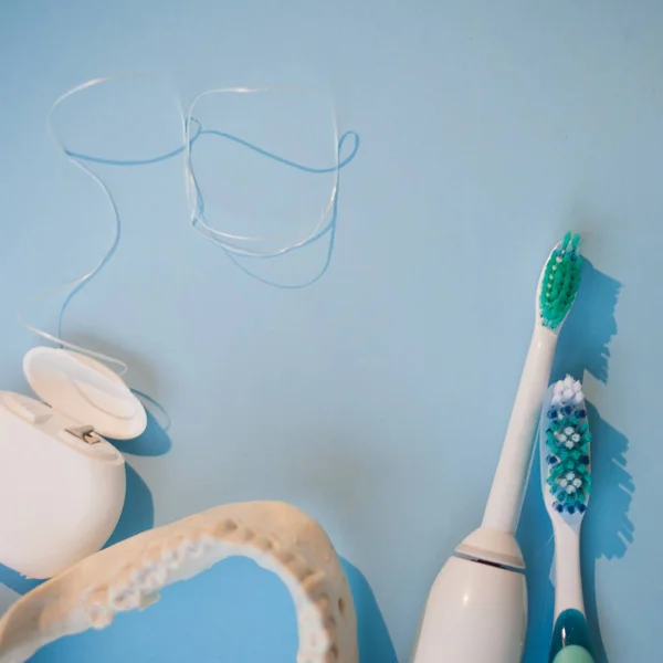 Cepillos, modelo de mandíbula y hilo dental sobre fondo azul —  Fotos de Stock