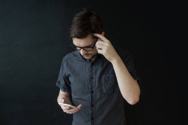 Gri gömlekli bir genç yetişkin adam bir akıllı telefon kullanır. İş portre dokulu siyah arka plan üzerine