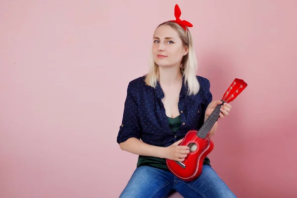 Portrét elegantní Mladá blondýnka s ukulele. Žena s čelenkou na růžovém pozadí — Stock fotografie