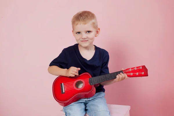 ピンクの背景の肖像画のギターを弾いている少年. — ストック写真