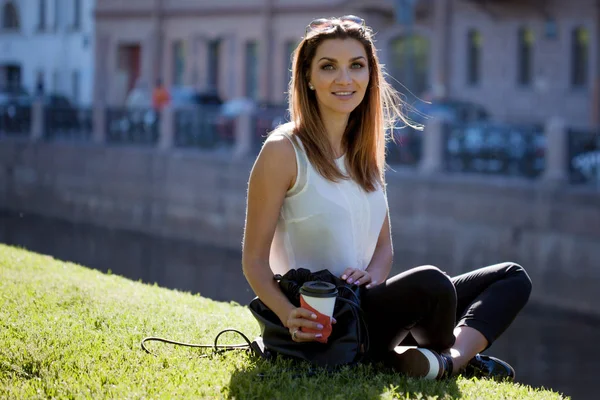 Женщина, сидящая на траве и пьющая кофе в картонной чашке — стоковое фото