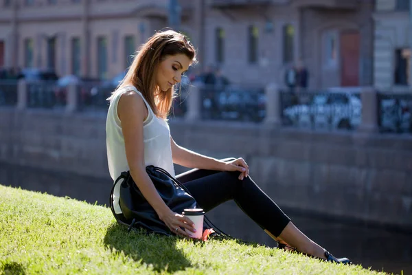 Mujer sentada en la hierba bebiendo café en una taza de cartón — Foto de Stock
