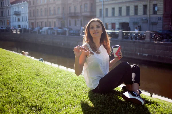 Žena sedí na trávě, pití kávy v lepenkové Cup — Stock fotografie