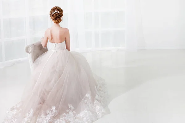 A noiva ruiva bonita senta-se na cadeira, penteado elegante, visão traseira. Jovem mulher em vestido de casamento luxuoso . — Fotografia de Stock