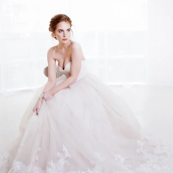 Porträtt av en vacker flicka i en bröllopsklänning. Bruden i lyxig klänning sitter på en stol — Stockfoto