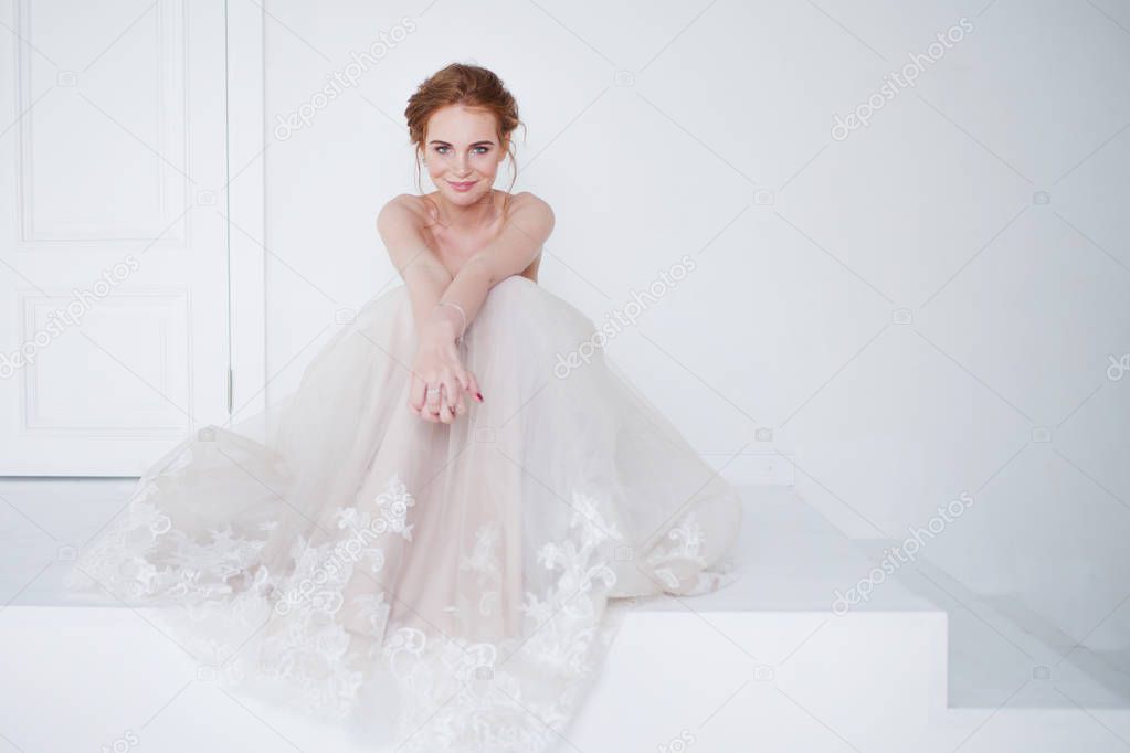 Portrait of a beautiful girl in a wedding dress. Bride in luxurious dress sitting on the floor