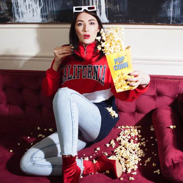 Mujer joven con capucha roja, viendo películas en casa, con palomitas de maíz . — Foto de Stock