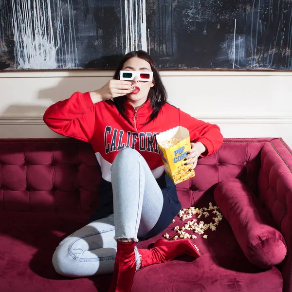 Jeune femme en sweat à capuche rouge, regardant des films à la maison, avec du pop-corn . — Photo