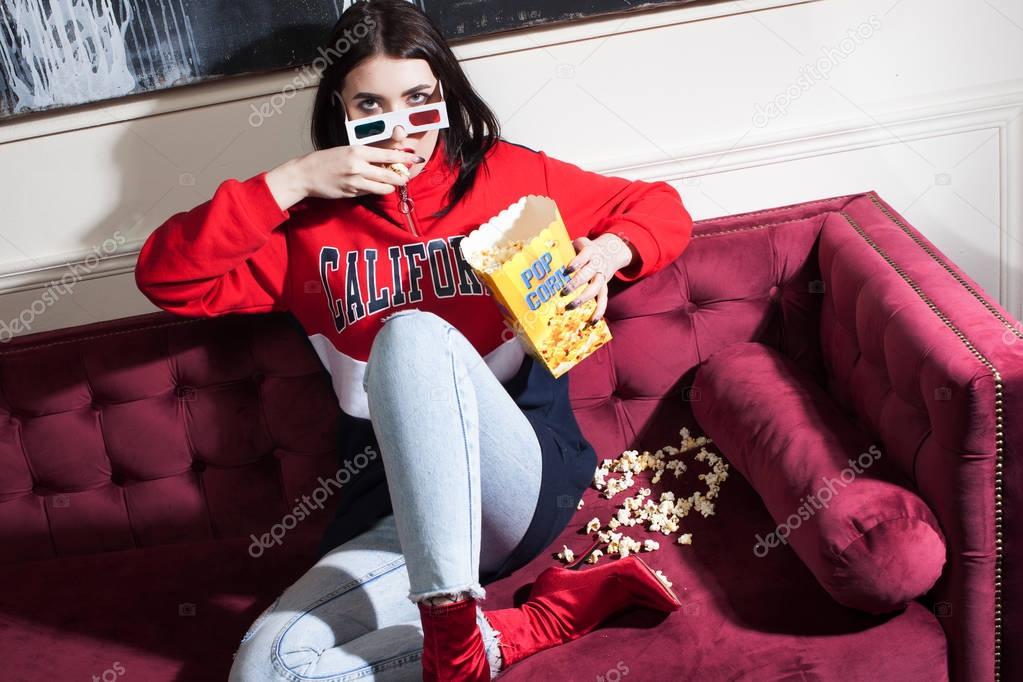 Young woman in a red hoodie, watching movies at home, with popcorn.