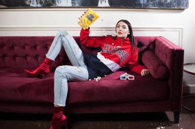 Evde film izlerken patlamış mısır ile kırmızı kapüşonlu genç kadında.