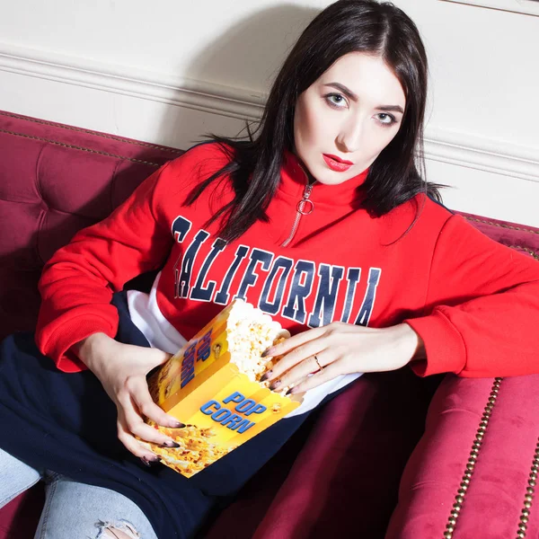 Mujer joven con capucha roja, viendo películas en casa, con palomitas de maíz . —  Fotos de Stock