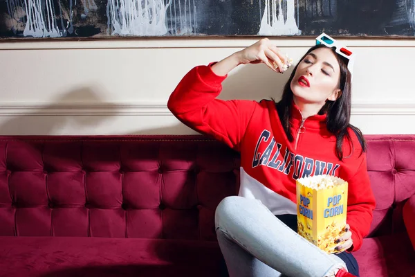 Mujer joven con capucha roja, viendo películas en casa, con palomitas de maíz . — Foto de Stock