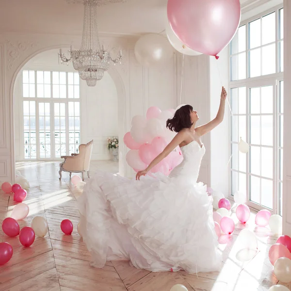 Mujer joven en vestido de novia en el interior de lujo vuela en globos rosados y blancos . — Foto de Stock