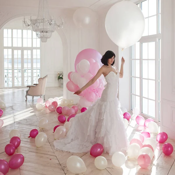 Junge Frau im Hochzeitskleid in luxuriösem Interieur mit einer Masse aus rosa und weißen Luftballons. — Stockfoto