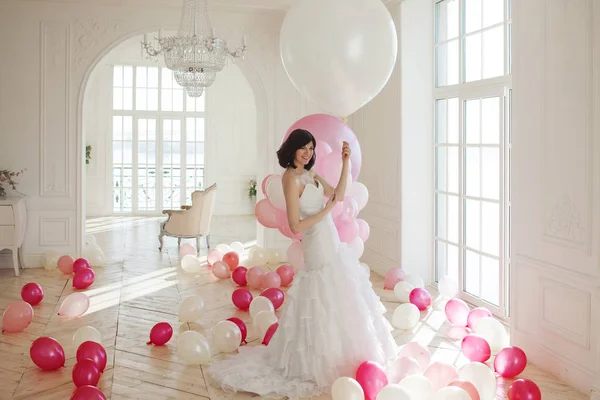 Giovane donna in abito da sposa in interni di lusso con una massa di palloncini rosa e bianchi . — Foto Stock