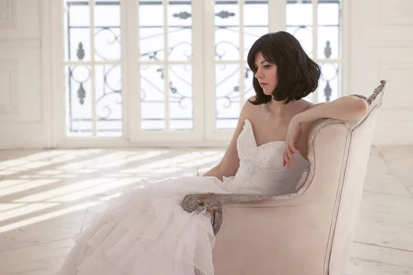 Junge Frau im Hochzeitskleid in luxuriösem Interieur sitzt vor dem Fenster — Stockfoto