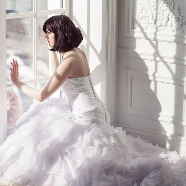 Retrato de jovem morena atraente com cabelo curto em um vestido de noiva. Sentado perto da janela, vista traseira . — Fotografia de Stock
