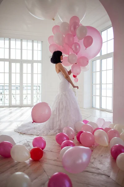 Jeune femme en robe de mariée à l'intérieur de luxe avec une masse de ballons roses et blancs . — Photo