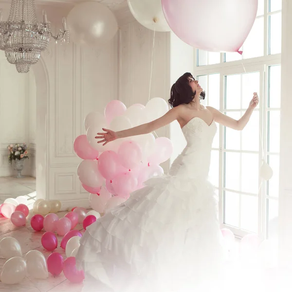 Junge Frau im Hochzeitskleid im luxuriösen Interieur fliegt auf rosa und weißen Luftballons. — Stockfoto