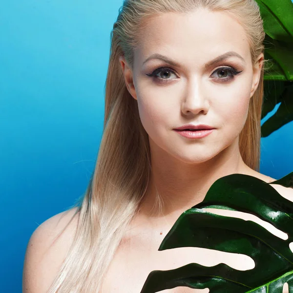 Twarz atrakcyjna Młoda Blondynka i liści drzew palmowych. Młoda kobieta w bikini niebieskie na niebieskim tle. — Zdjęcie stockowe