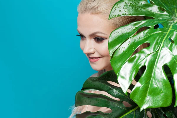 Обличчя привабливої молодої блондинки і листя пальмових дерев. Молода жінка в блакитному бікіні на синьому фоні . — стокове фото