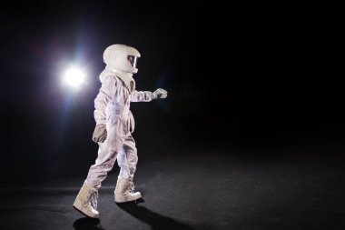 Astronot siyah bir zemin üzerine ileri gider ve bir yere el uzanır