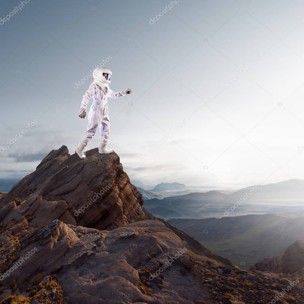 Portrait of astronaut in a space suit. Futuristic astronaut on the planet, standing on top of a mountain and stretches his hand away