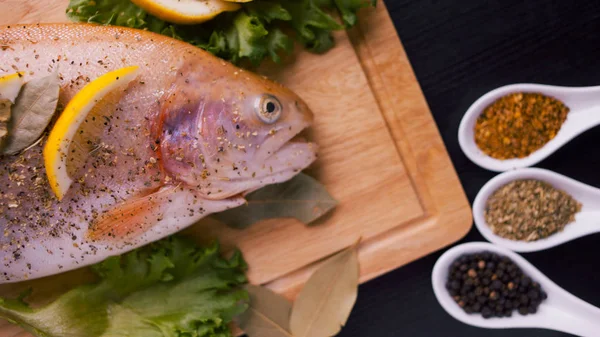 Frische Forellen und Zutaten für Fischgerichte auf schwarzem Tisch — Stockfoto