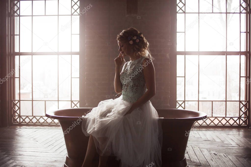Young bride in dress, silhouette on window background. sits against the light.