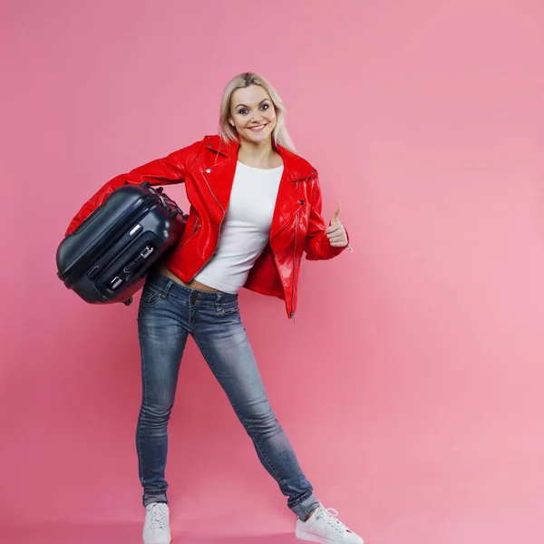 Koncept, redo att resa. Ung kvinna med resor resväska visar tummen. Blond turist flicka på rosa bakgrund — Stockfoto