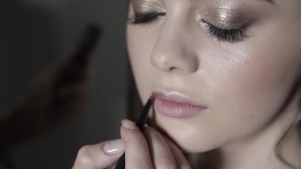 Maquillaje artista aplicar lápiz labial con un cepillo. Chica joven haciendo maquillaje profesional — Vídeo de stock