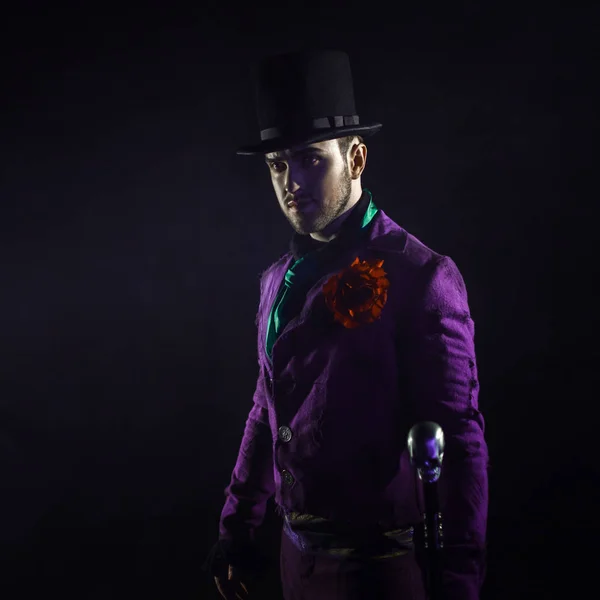 Mysterious man in a suit, with a cane, in a cylinder. Dark background. Scary and sinister. Joker, Halloween costume — Stock Photo, Image