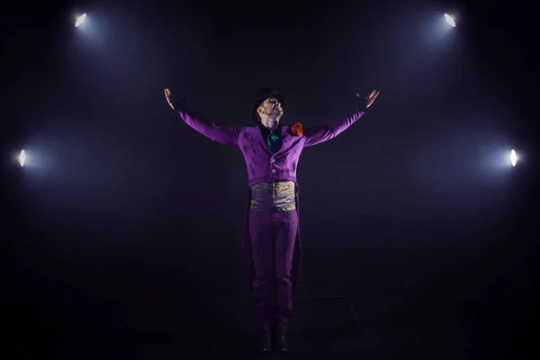 Young man in purple suit standing on the background of the spotlight. Showman raised hand, show begins — Stock Photo, Image