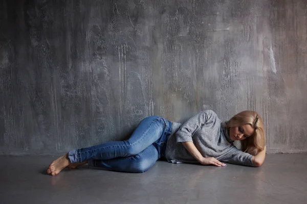 Traurige Frau auf dem Boden liegend. Depressionen und chronische Müdigkeit. junge schöne Blondine in grauem Pullover und Jeans — Stockfoto