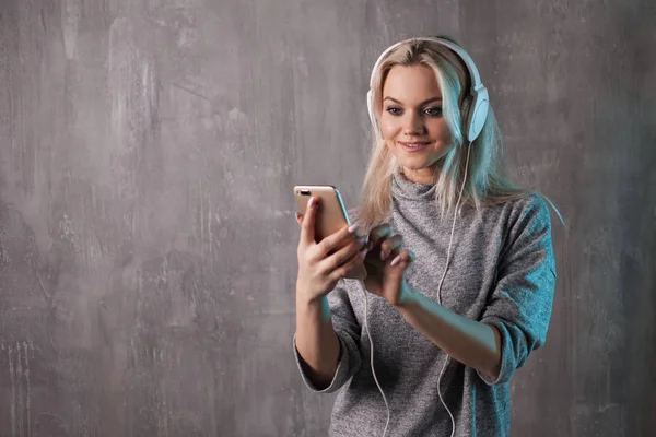 Jovem encantadora usando smartphone e fones de ouvido grandes — Fotografia de Stock