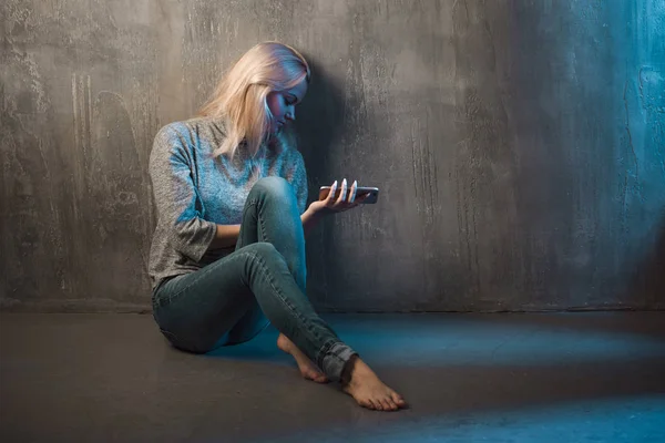 Triest jonge vrouw zittend op de vloer met een telefoon in handen. Bel te wachten, geen verbinding. — Stockfoto