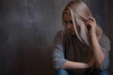 Duvara oturan üzgün genç kadın. Genç sarışın. Depresyon ve sorunları